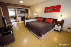 A hotel room with a bed, bedside table, lamp, and a view of the kitchen and living area. - Standard Studio - Ayres Apartments Uriburu (Buenos Aires)