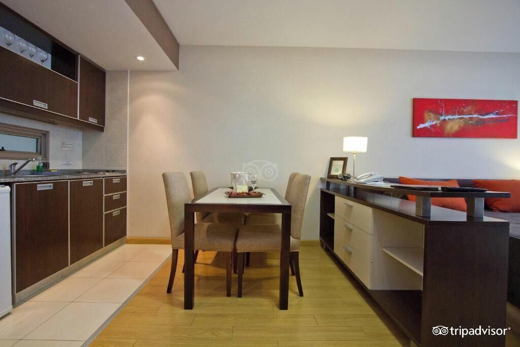 A modern kitchen with dark cabinetry, a dining area with a table and chairs, and a sofa with cushions.