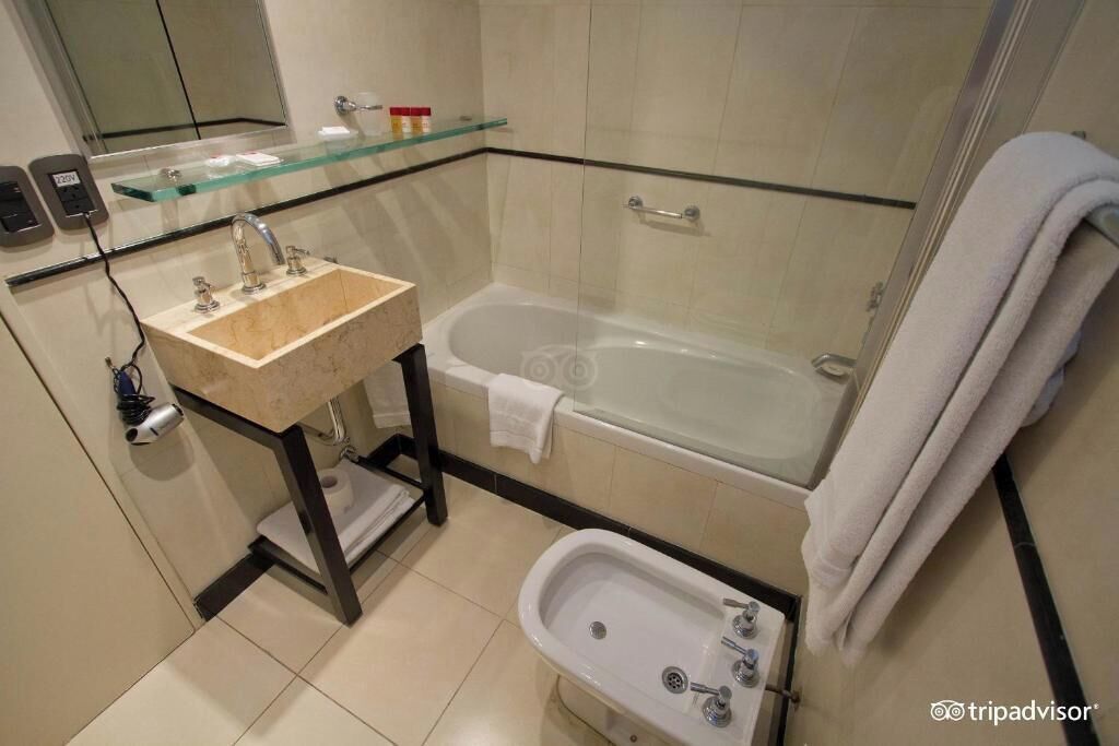 A modern bathroom with a glass shelf, a sink, a bathtub, and a bidet.