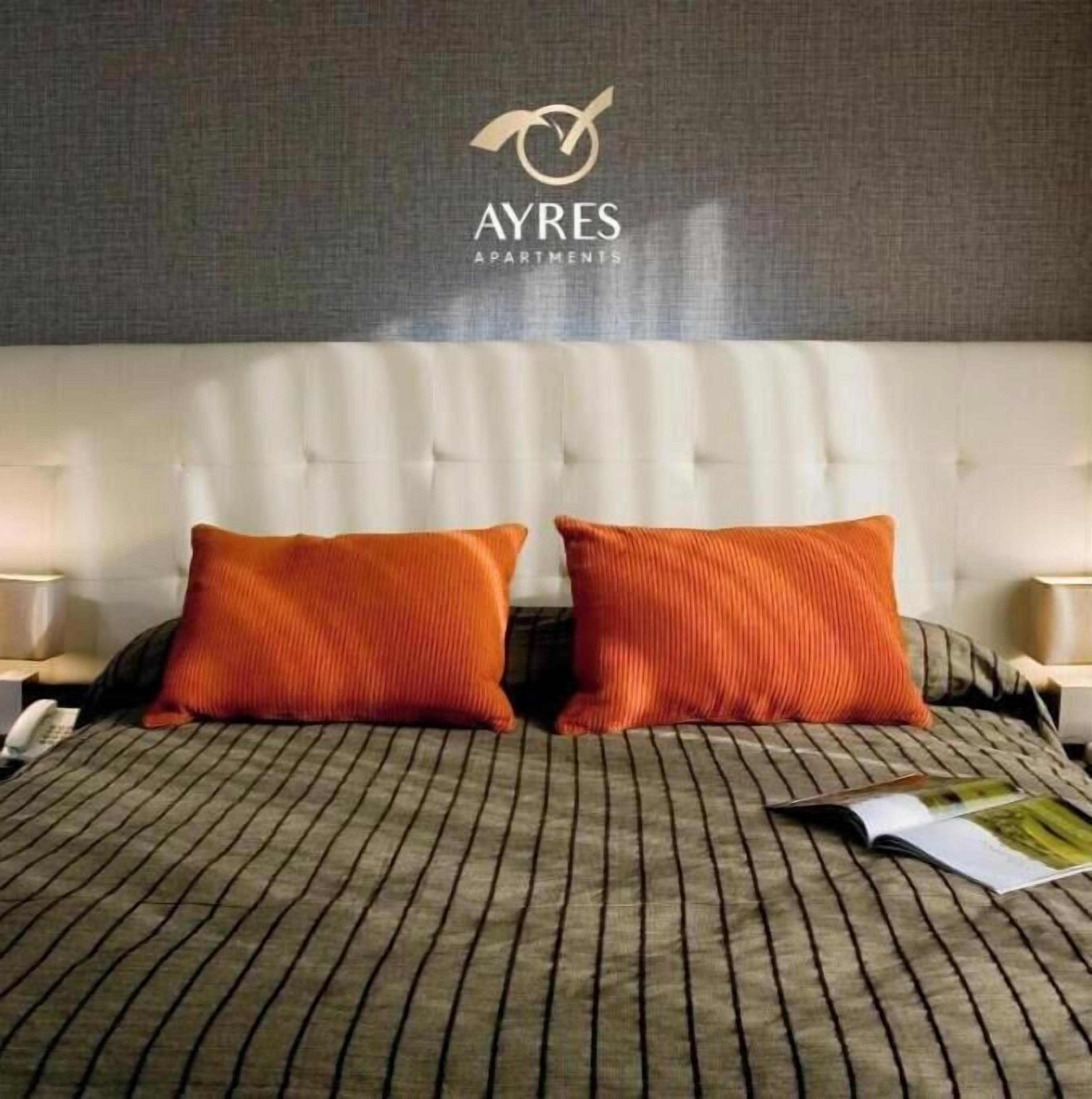 A bedroom with a tufted headboard, two orange pillows, and a striped bedspread.