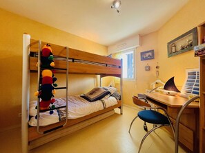 Cozy dorm room with a bunk bed, desk, and shelf, perfect for a simple stay.