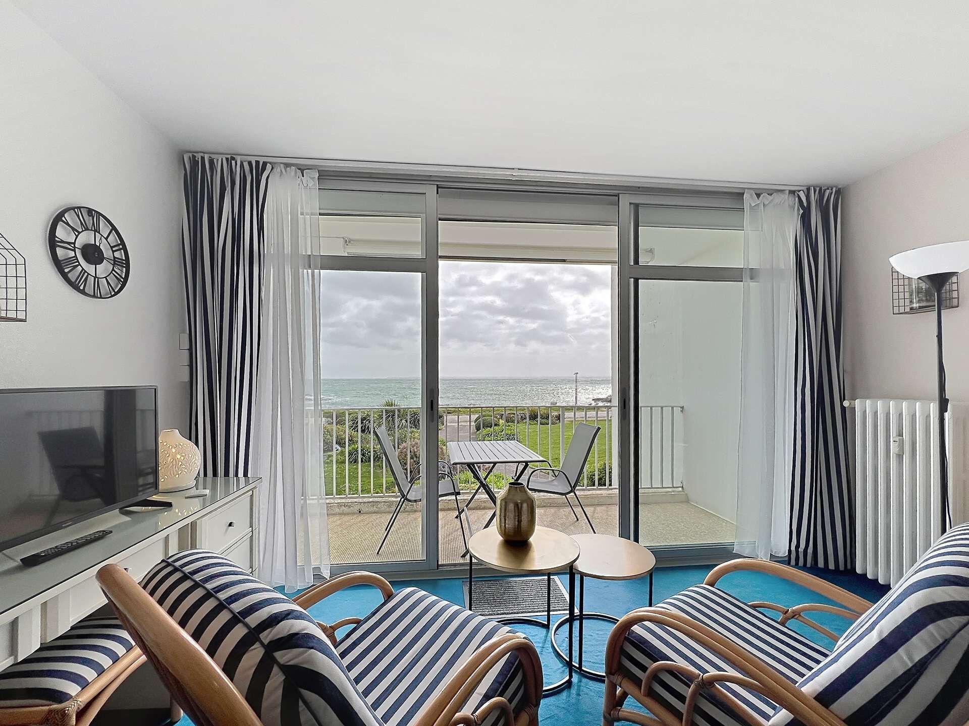 Een balkon met uitzicht op zee, een televisie en gestreept meubilair.