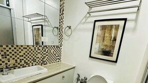 Een badkamer met een witte wastafel, een toilet, een blauwe prullenbak en een fotokader aan de muur.