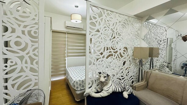 Een moderne woonkamer met een decoratieve witte scheidingswand, een bank, een bed met beddengoed met een patroon en een tijgerknuffel.