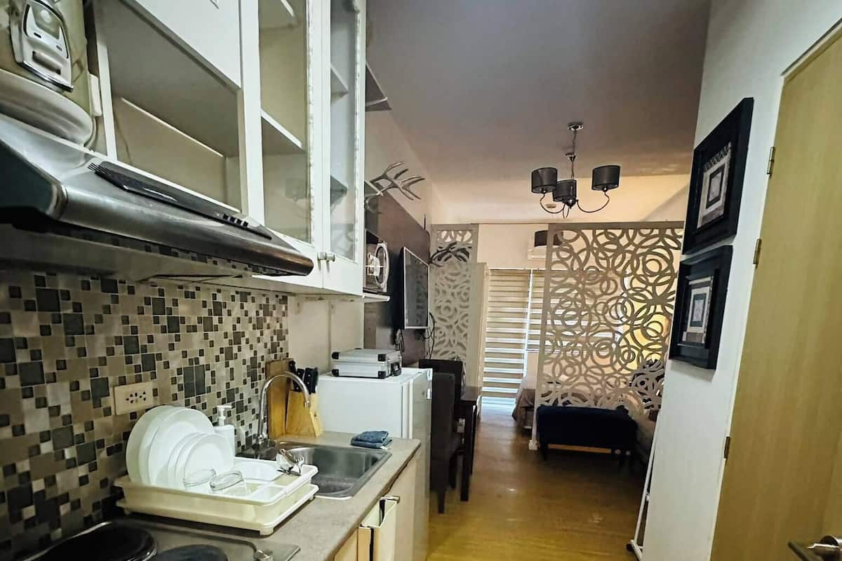 Een smalle keuken met een betegelde spatwand, een kookplaat en een spoelbak. Er is een patroon op de muur en een deur naar een andere kamer.
