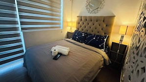 Een opgemaakt bed met hoofdbord, bedlampje en een wandklok.