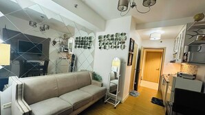 Een moderne woonkamer met een bank, een televisie en een keukenhoek met kasten en apparatuur.