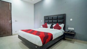 A bedroom with a bed, a nightstand, a telephone, and a door. - Hotel Pingla Residency  (New Delhi)