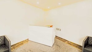 A reception area with a white desk, two black chairs, and a carpeted floor. - Hotel Pingla Residency  (New Delhi)