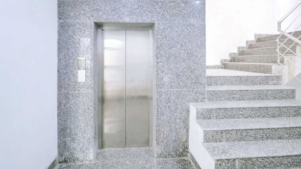 A modern elevator with a metallic finish, adjacent to a staircase with granite steps and metal railings. - Hotel Pingla Residency  (New Delhi)