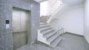 A modern elevator with a control panel, a staircase with metal railings, and a granite floor. - Hotel Pingla Residency  (New Delhi)