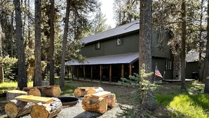 A rustic lodge with a covered porch, log seating, and a stone fireplace. - Family Retreat 29 Miles to Yellowstone in a Quiet Wooded Area, with a Kids Nook (Island Park)