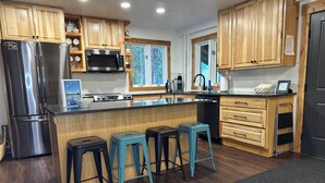 A modern kitchen with wooden cabinets, stainless steel appliances, and a central island with bar stools. - Family Retreat 29 Miles to Yellowstone in a Quiet Wooded Area, with a Kids Nook (Island Park)
