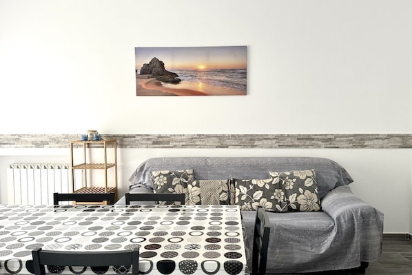 A room with a bed, a table, and a wall-mounted painting of a sunset over the ocean.
