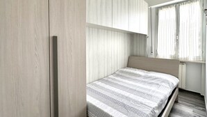 Un dormitorio con cama, armario y ventana con cortinas.