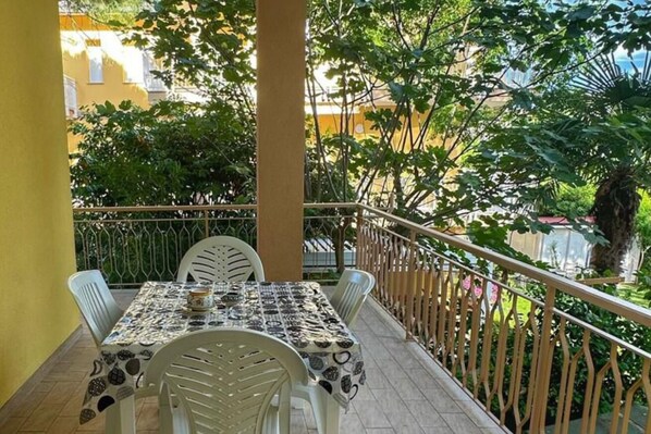 A balcony with a table and chairs, surrounded by greenery and buildings.