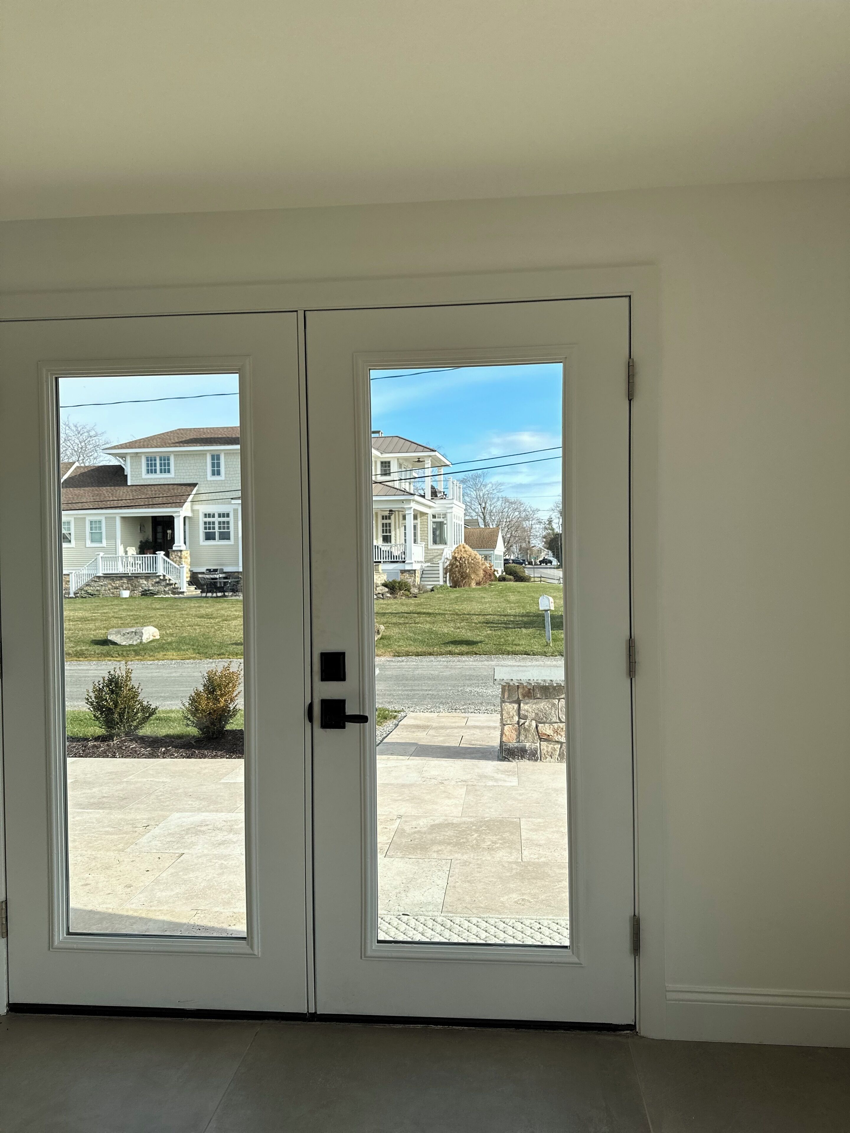 A double door leading to a driveway with a lawn and a house in the background.
