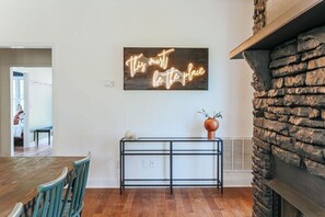 Ein Essbereich mit Holztisch und Stühlen, einem Neonlichtschild an der Wand und einem Steinkamin.