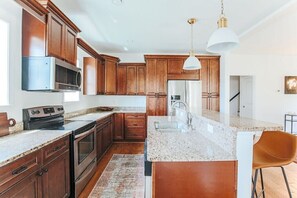 Una cocina con armarios de madera, electrodomésticos de acero inoxidable, encimera de granito e iluminación colgante.