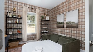 Een slaapkamer met ruitjesbehang, een bed met witte lakens, een groene bank en twee aan de muur bevestigde foto's.