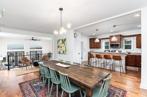 Un comedor amplio con mesa y sillas de madera, una cocina con taburetes de bar y vistas al exterior.