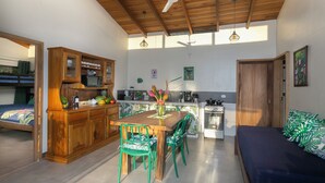 Cocina compacta con armarios de madera, una mesa de comedor con sillas, una kitchenette y un área de descanso con cama.