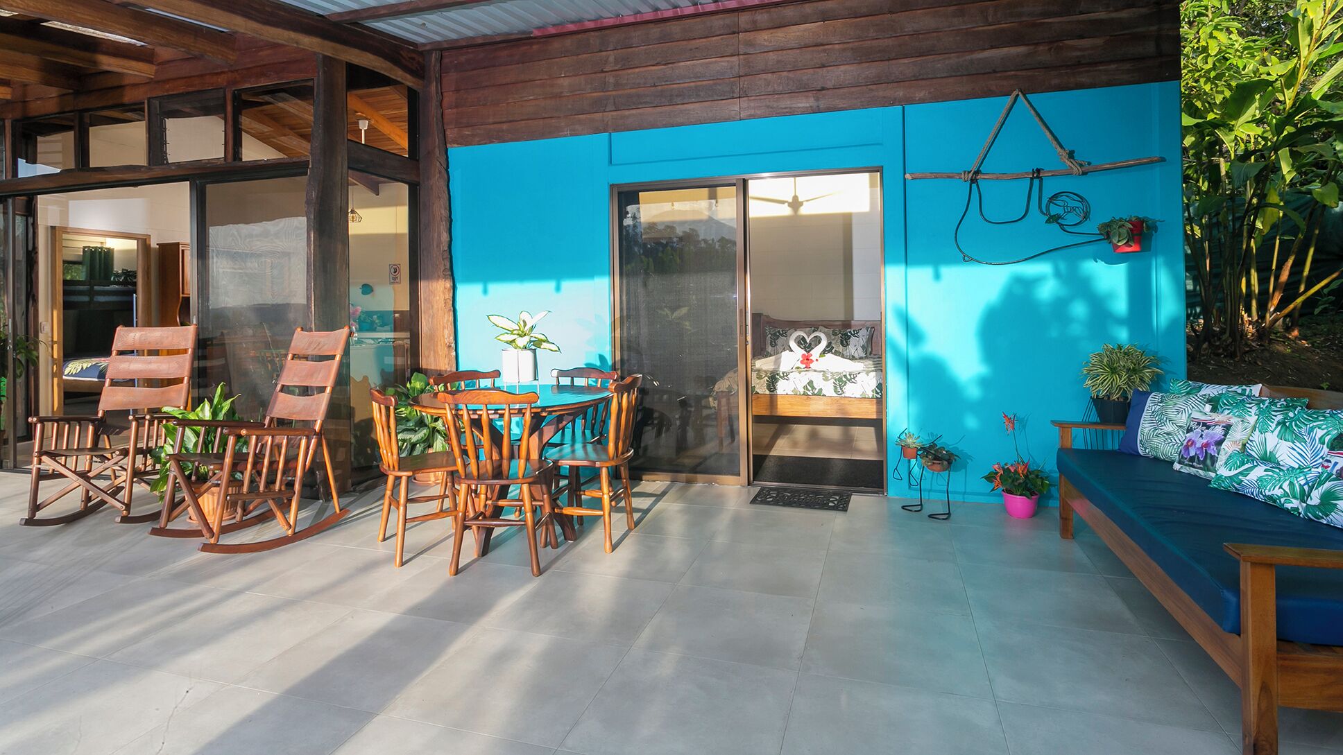 Un espace patio avec une table et des chaises en bois, un mur bleu et des plantes en pot.