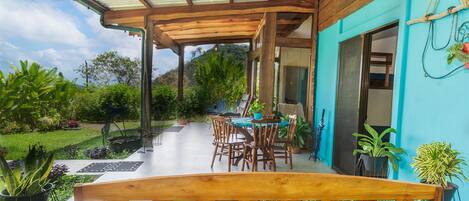 An outdoor patio with a wooden table and chairs, surrounded by potted plants and a view of the garden.