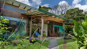 Una casa moderna con un porche cubierto, un mural en la pared exterior y un jardín con diversas plantas y flores.