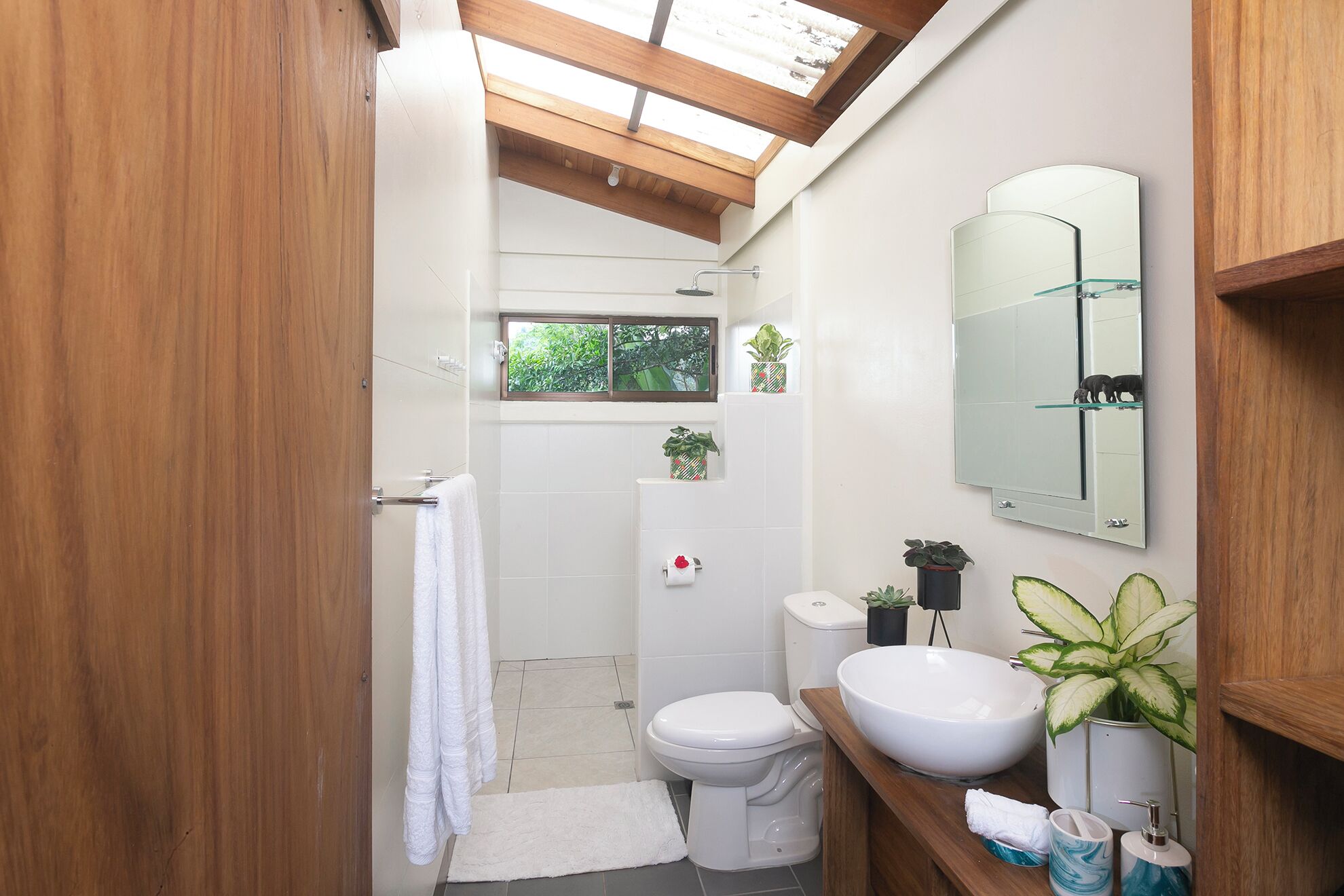 Ein modernes Badezimmer mit Oberlicht, weißen Armaturen und Topfpflanzen.