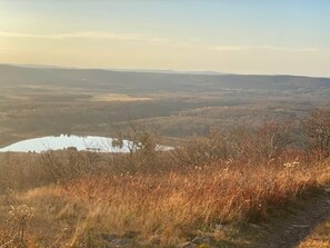 Une vue panoramique d’un paysage vallonné, avec un lac et un sentier qui traverse le premier plan.