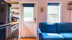 A compact living space with a kitchenette, a washing machine, a blue sofa, and two windows with blue blinds. - Stunning seaside studio, walk to beach, romantic getaway for 2  (Plymouth)