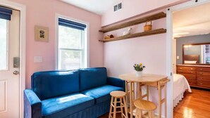 A room with a blue sofa, wooden stools, a small table, and a kitchen area with wooden cabinets and a sink. - Stunning seaside studio, walk to beach, romantic getaway for 2  (Plymouth)
