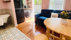 A compact living space with a kitchenette, a sofa, a dining table, and a washing machine. - Stunning seaside studio, walk to beach, romantic getaway for 2  (Plymouth)