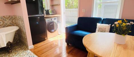 Ett kompakt bostadsutrymme med ett litet kök, en soffa, ett matbord och en tvättmaskin.