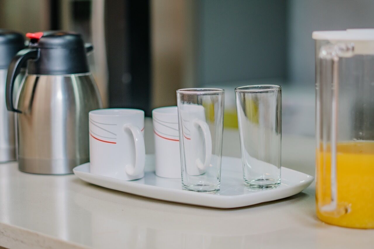 A kitchen counter with a coffee maker, two white mugs, and two clear glasses.