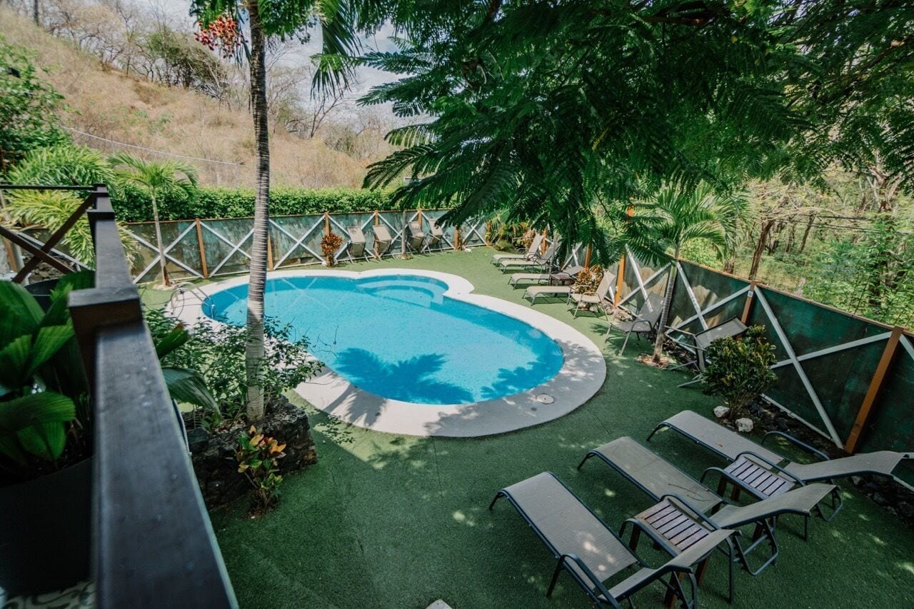 Piscina con sillas de descanso y un área cercada, rodeada de vegetación.