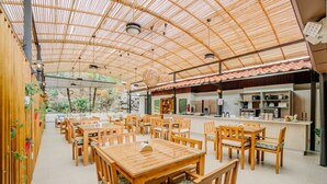 Un amplio comedor interior con mesas y sillas de madera, una cocina con electrodomésticos modernos y un techo de bambú.