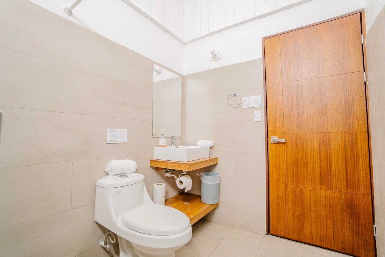 A small bathroom with a toilet, sink, and mirror. There is a wooden door and a trash can.