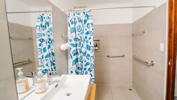 A bathroom with a shower, a sink with soap dispensers, and a wooden bench.