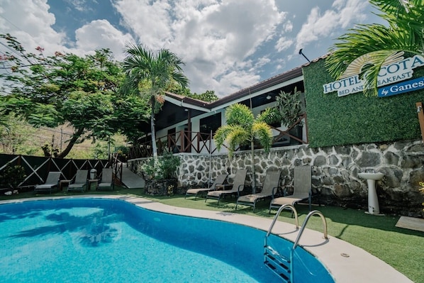 A hotel with a swimming pool, lounge chairs, and a sign indicating it offers breakfast. - Hotel Ocotal B&B (Sardinal)