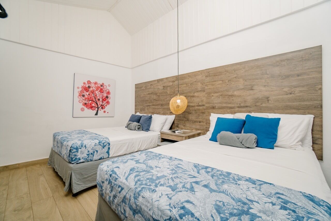 Een hotelkamer met twee bedden, een houten hoofdeinde, een hanglamp en een kunstwerk aan de muur.