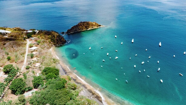 Vista aérea de una zona costera con aguas turquesas cristalinas, una playa de arena y varios barcos.