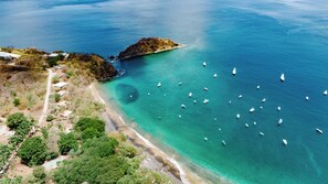 An aerial view of a coastal area with clear turquoise waters, a sandy beach, and several boats. - Hotel Ocotal B&B (Sardinal)