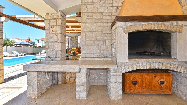 An outdoor kitchen area with a stone fireplace, a pool, and lounge chairs. - House 2326/110968 (Istria - Vodnjan), 5000m from the beach (Vodnjan)