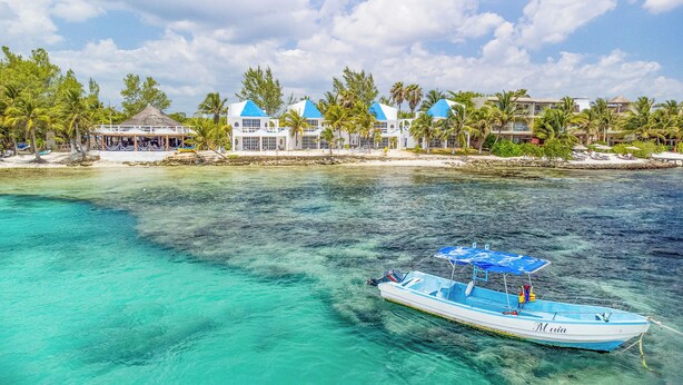 A boat anchored near a resort with clear turquoise water, a beach, and palm trees. - Casa Cenote Hotel (Tulum)