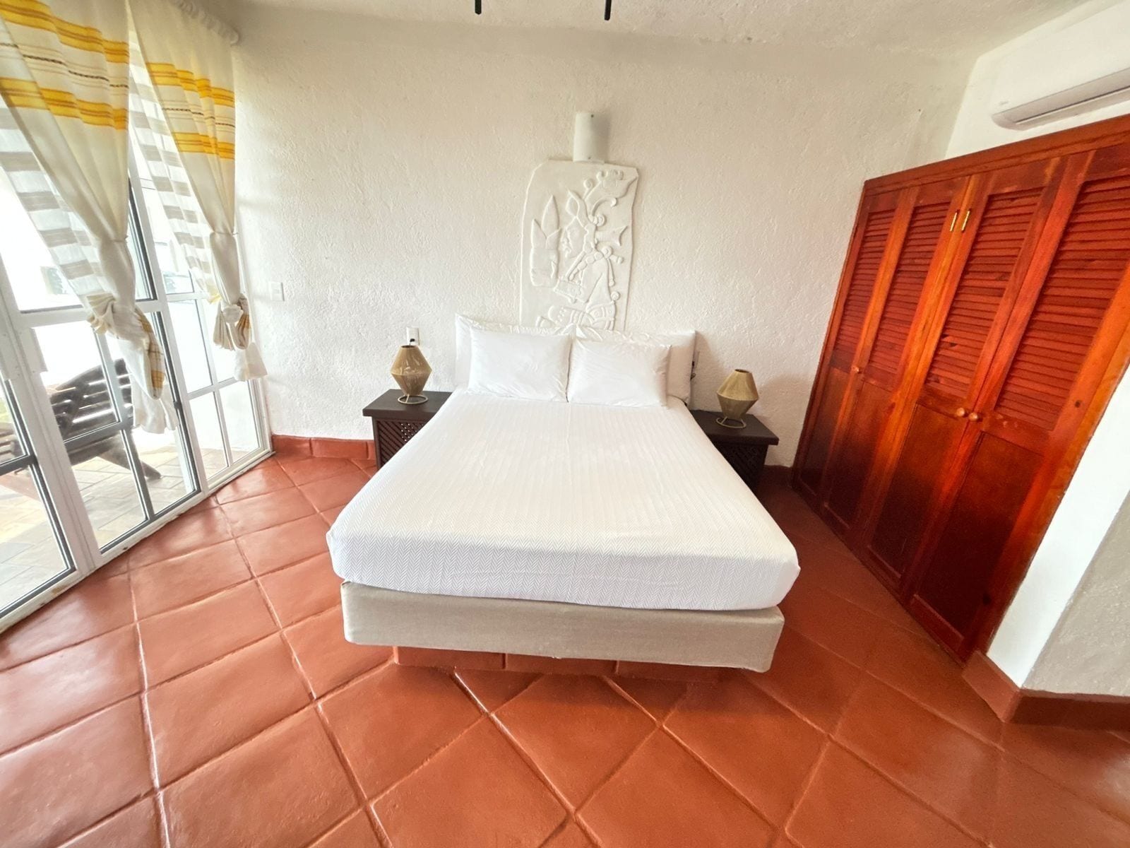 Quarto com uma cama grande, uma porta de correr de vidro, um guarda-roupa de madeira e uma peça decorativa na parede.