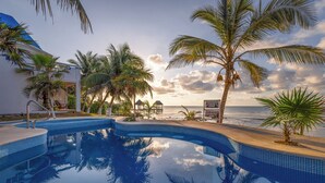 A swimming pool with clear blue water, surrounded by palm trees and a view of the ocean. - Casa Cenote Hotel (Tulum)