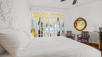 Una habitación de hotel con cama, ventilador de techo, una silla de madera y una ventana con cortinas.