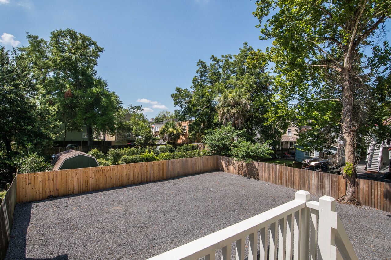 A backyard with a wooden fence, gravel surface, and trees.